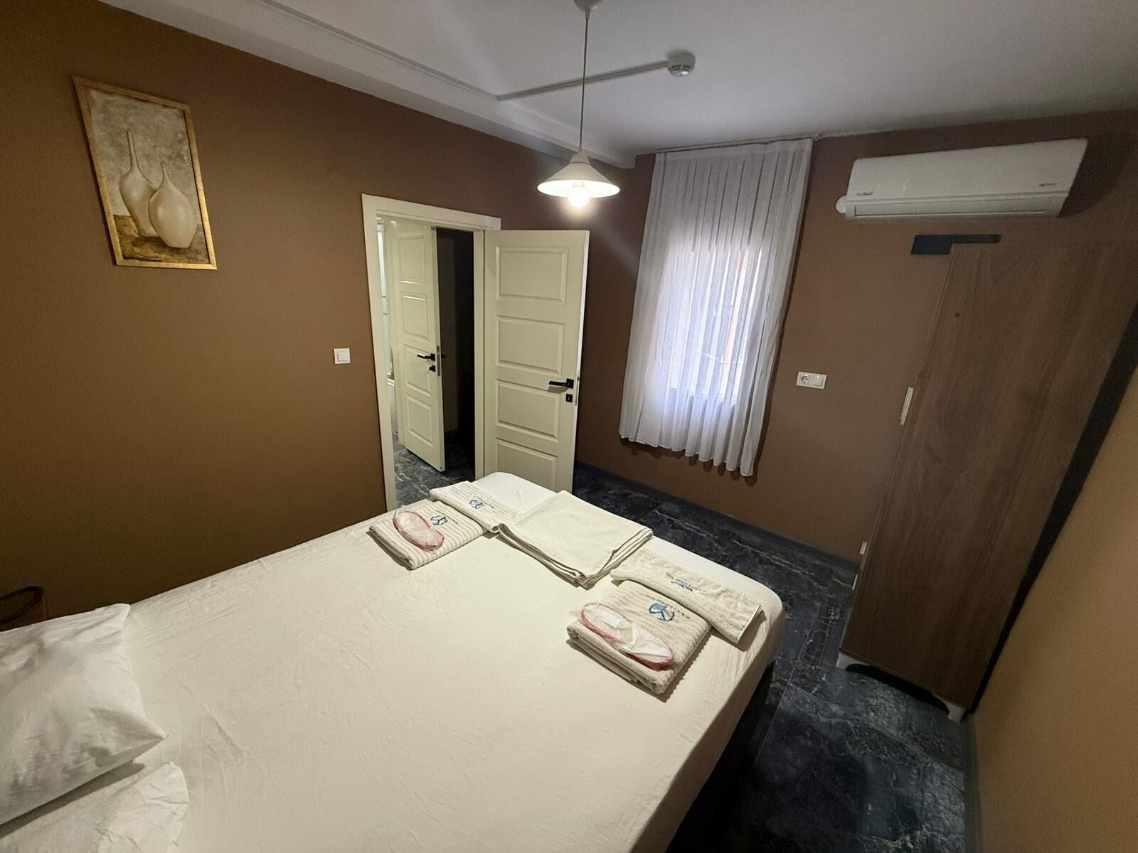 Una camera d'albergo con un letto, una porta, una finestra con tende e un condizionatore d'aria.