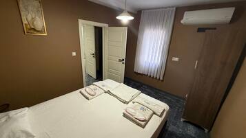 Una camera d'albergo con un letto, una porta, una finestra con tende e un condizionatore d'aria.