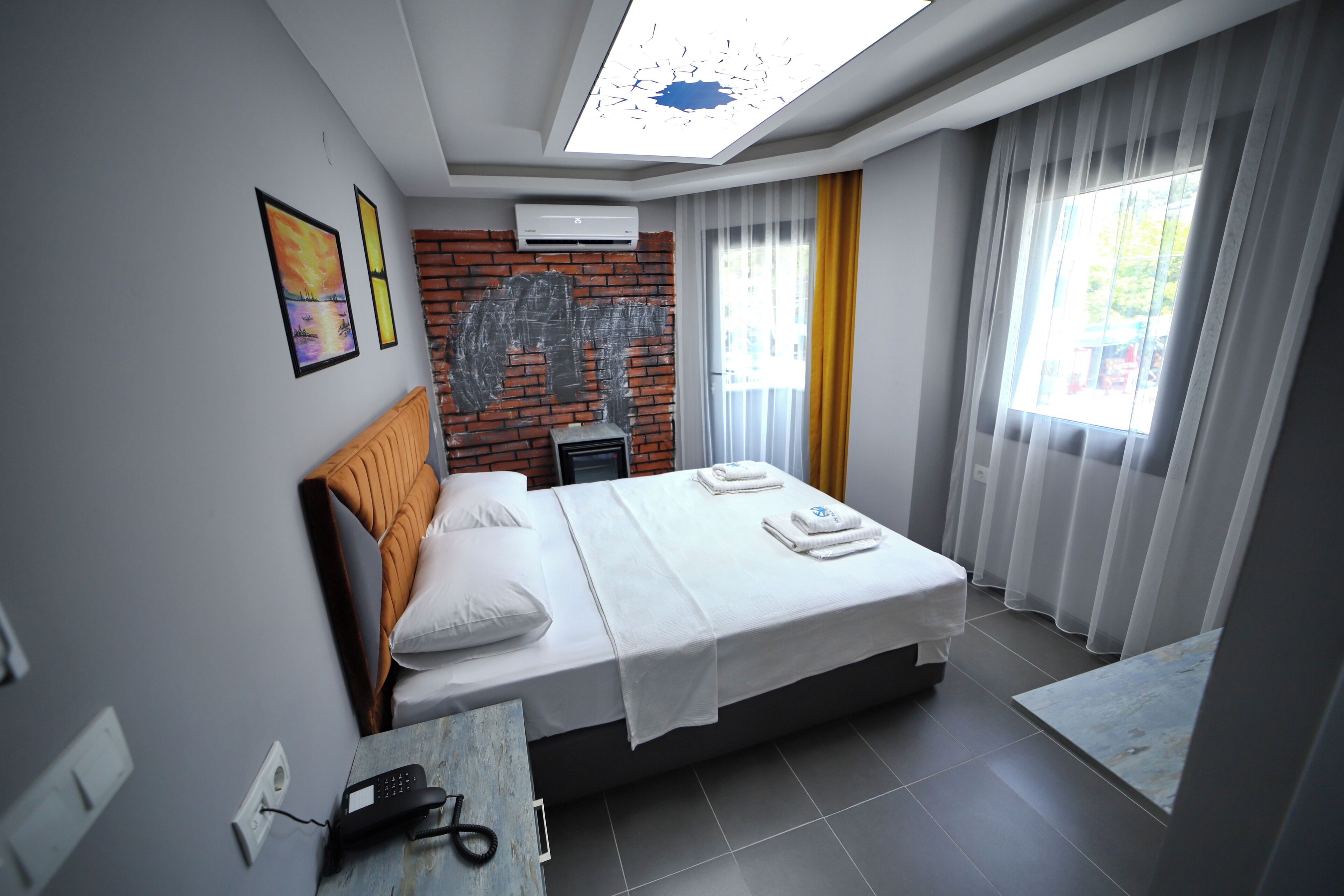 A modern hotel room with a large bed, a desk, a chair, a skylight, and a brick accent wall.