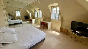 Un dormitorio con cama, escritorio, silla, televisor y un espejo grande.