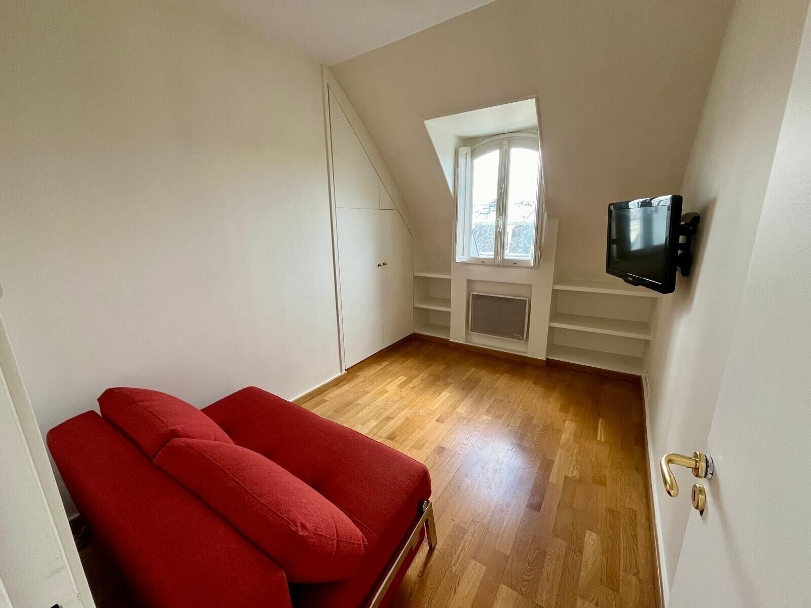 A room with a red sofa, a television, a window, and a door.