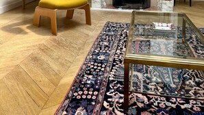 Una sala de estar moderna con chimenea, un sillón amarillo, una mesa de centro de vidrio y una alfombra estampada.