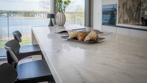A modern kitchen with a marble countertop, a vase with green flowers, and a tray of pastries. - Apartamenty Kapitańska by Elite4Rent (Olsztyn)
