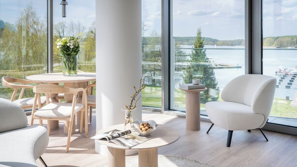 A modern room with a large window, a round table, a white armchair, and a vase with flowers. - Apartamenty Kapitańska by Elite4Rent (Olsztyn)