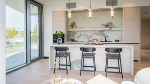 A modern kitchen with a marble backsplash, a large window, and a bar area with three stools. - Apartamenty Kapitańska by Elite4Rent (Olsztyn)