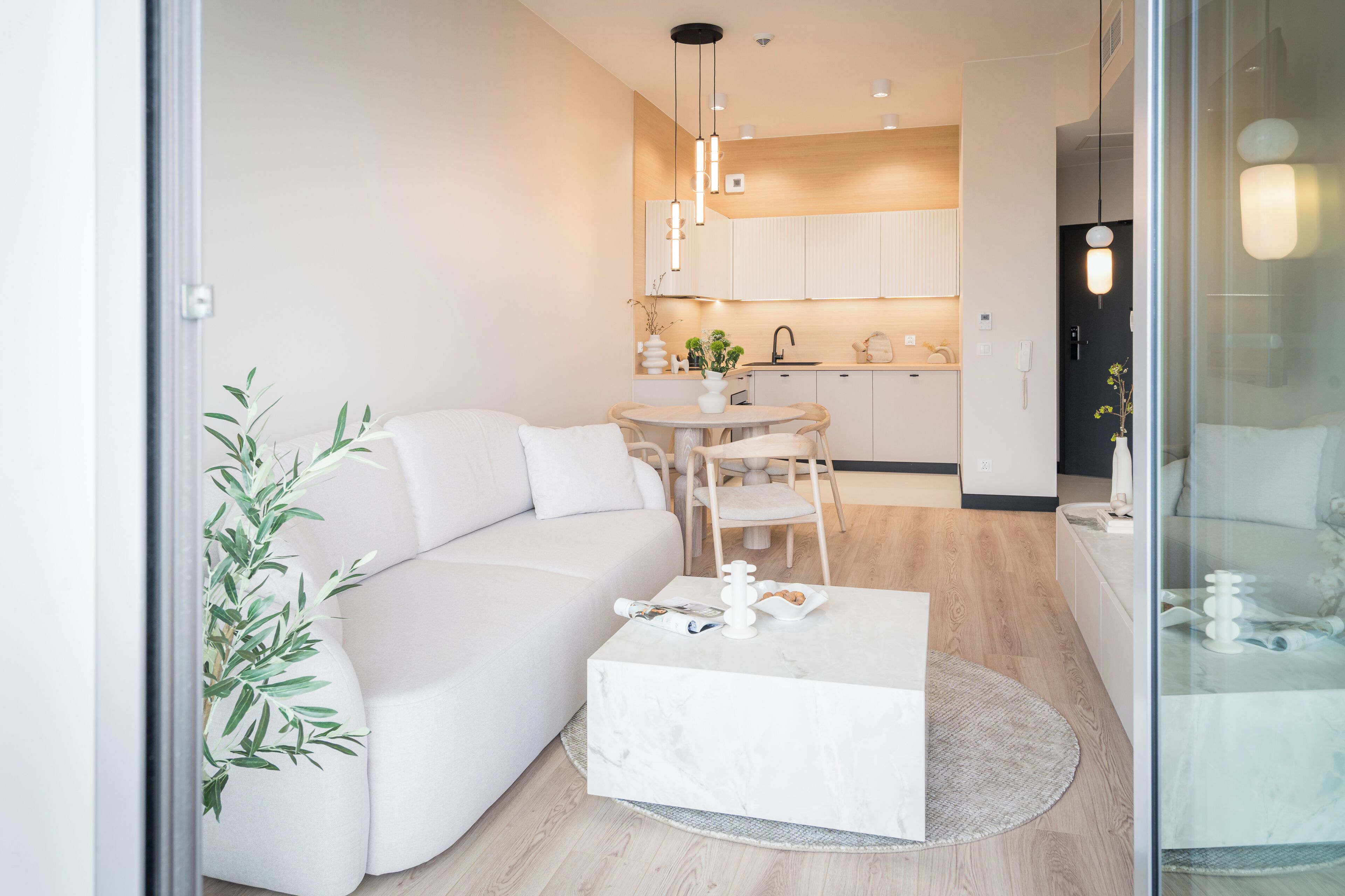 A modern living room with a white sofa, a round coffee table, and a dining area with a wooden table and chairs.
