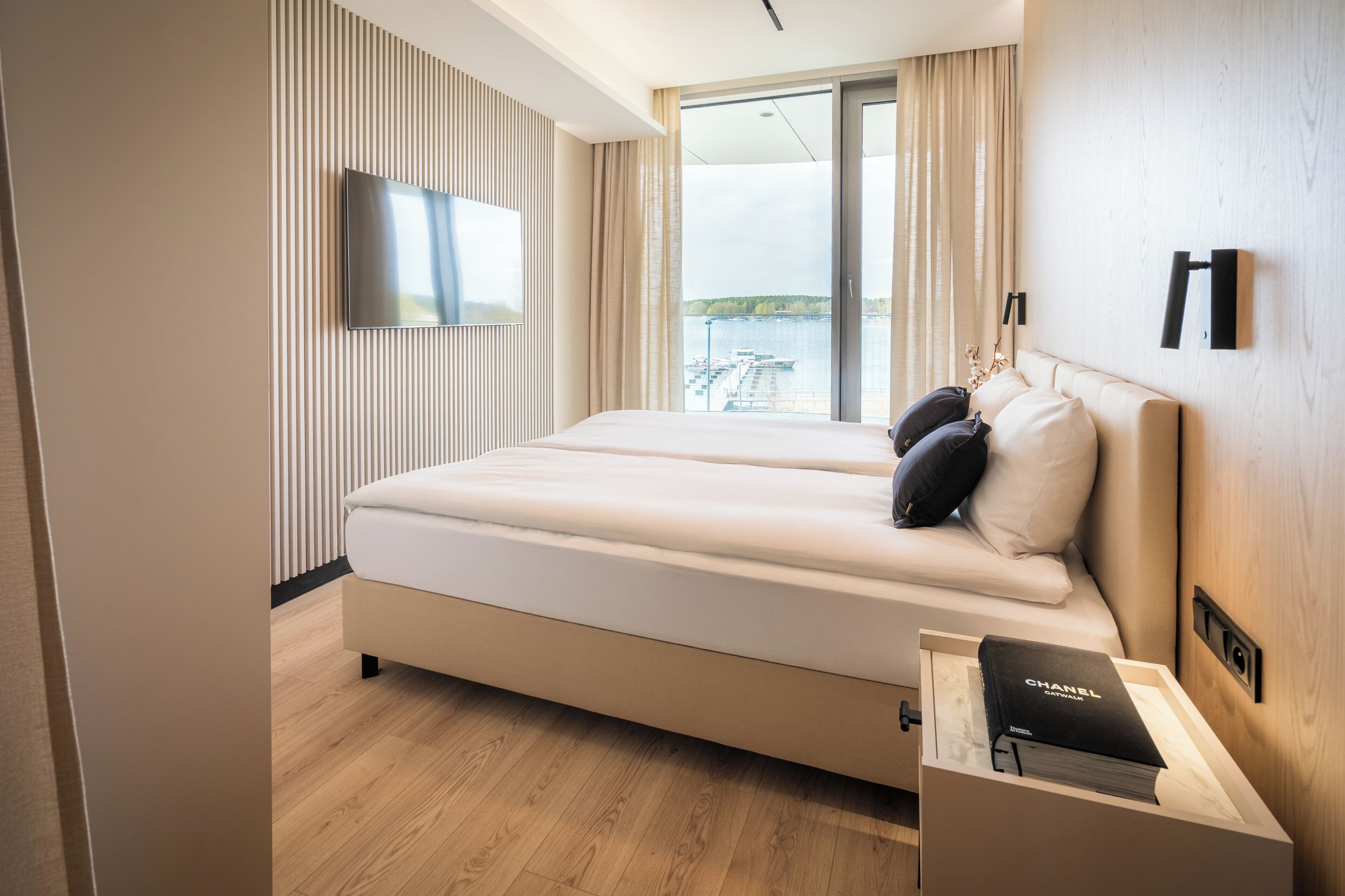 Camera d'albergo moderna con un letto grande, una TV a parete e vista su un corpo d'acqua.