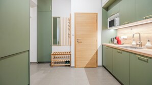 Cocina compacta con gabinetes verdes, una puerta de madera, un microondas, un lavamanos y un zapatero.