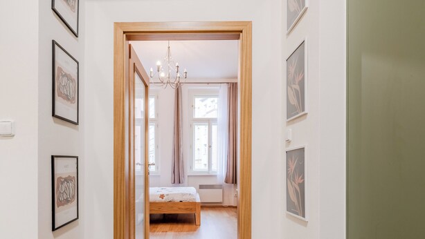 Un pasillo que conduce a un dormitorio con una cama, cuadros en las paredes y una puerta de madera.
