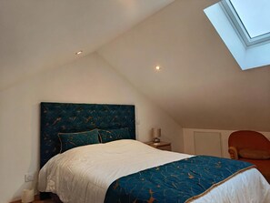 Une chambre avec un plafond en pente, un lit avec une tête de lit bleue, une table de chevet, une lampe et une chaise.