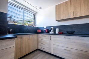 A modern kitchen with a large window, wooden cabinets, and a black countertop. - Gîte La Sagnette 4/6 persons (LANUEJOLS)