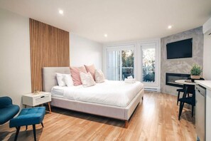 A modern bedroom with a bed, bedside table, chair, and a TV mounted on the wall. - LAO LOFT 106 by Gestion ELITE (Mont-Tremblant)