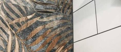 Une salle de bain dotée d’une douche au design moderne, d’un mur décoratif recouvert de carreaux et d’un plafond apparent.