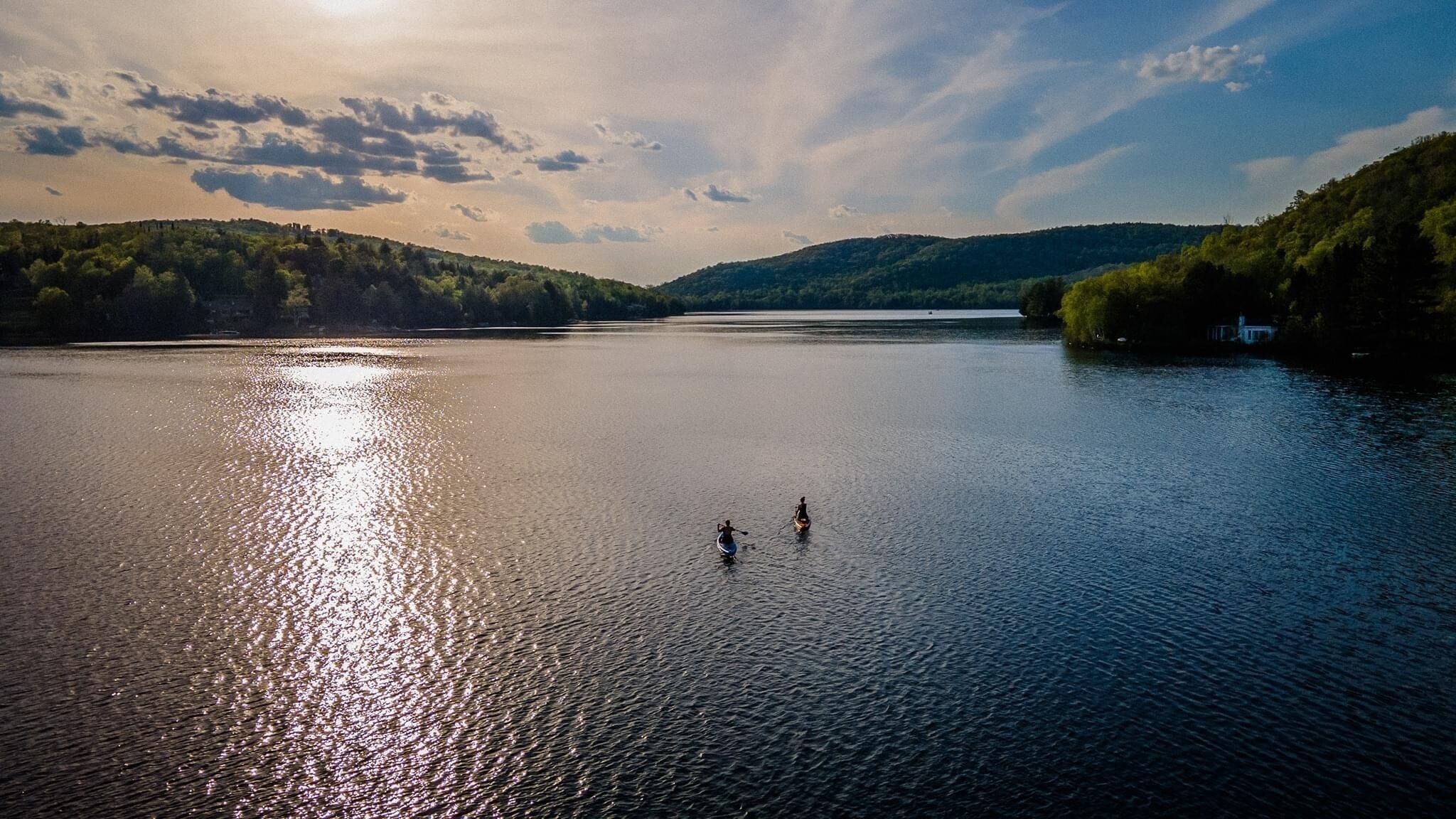 Un lago tranquilo con dos botes a pedal, rodeado de colinas boscosas.