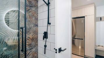 A modern bathroom with a glass shower enclosure, a built-in toilet, and a stainless steel refrigerator.