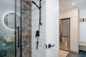 A modern bathroom with a glass shower enclosure, a built-in toilet, and a stainless steel refrigerator. - LAO LOFT 106 by Gestion ELITE (Mont-Tremblant)