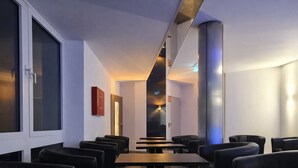 A modern interior with seating, tables, and a corridor leading to an exit. - Check-Inn Hotel - Offenbach (Offenbach am Main)