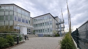 A modern building with large windows, a covered entrance, and a staircase leading to an upper level. - Check-Inn Hotel - Offenbach (Offenbach am Main)