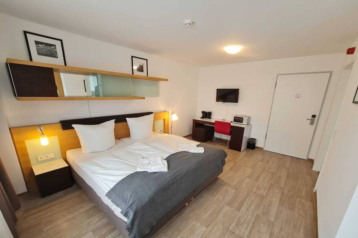 Une chambre d’hôtel avec un lit, des tables de chevet, un bureau, une télévision et une porte.