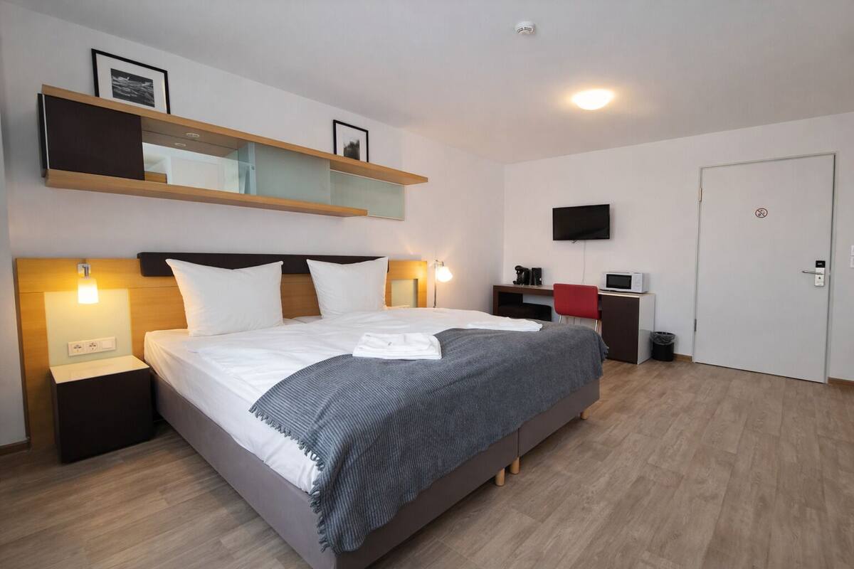 Une chambre d’hôtel moderne avec un grand lit, des tables de chevet, un téléviseur à écran plat, un bureau et une chaise rouge.