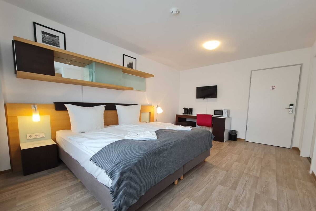Une chambre d’hôtel moderne avec un grand lit, des tables de chevet, une télévision, un bureau et un miroir.