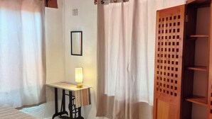 Un dormitori amb un llit, un escriptori amb una làmpada, un armari de fusta i una panxa.