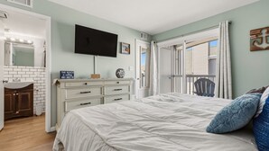 Un dormitorio con cama, televisión, cómoda, espejo y ventana.