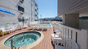Un área de piscina con sillones de descanso y un jacuzzi en una terraza de madera.
