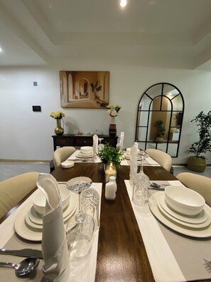 Comedor con una mesa de madera dispuesta para cuatro, platos blancos, vasos y un florero con flores.