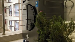 Quarto com um eletrodoméstico de estilo industrial, um vaso de planta e um corrimão de metal.
