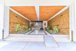 Una entrada moderna de edificio con techo de madera, mostrador de recepción y plantas en macetas.