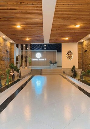 Un moderno vestíbulo de hotel con un mostrador de recepción central, paneles de techo de madera y un suelo reflectante.