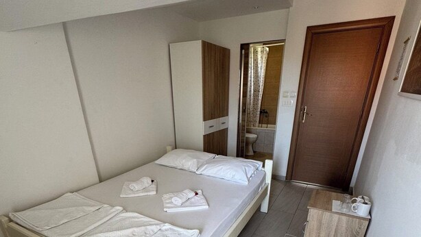 A single-bed room with a wooden headboard, a bedside table with a cup and a book, and a wooden door.
