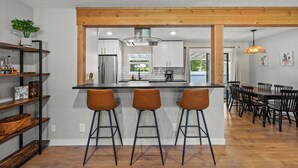 Een moderne keuken met een centraal eiland, barkrukken, en een eethoek met een houten tafel en stoelen.