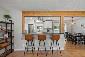 A modern kitchen with a central island, bar stools, and a dining area with a wooden table and chairs. - Spacious 4-bedroom House close to Lake Coeur d'Alene and Downtown (Coeur d'Alene)
