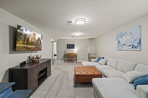 A living room with a flat-screen TV, a sofa, a coffee table, a desk, and a chair. - Spacious 4-bedroom House close to Lake Coeur d'Alene and Downtown (Coeur d'Alene)
