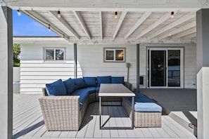 En uteplats med en flätad soffgrupp, ett litet bord och en pergola som ger skugga.