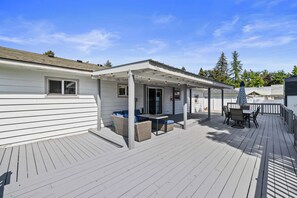 A covered outdoor deck with seating and a table, surrounded by a wooden deck and a white building. - Spacious 4-bedroom House close to Lake Coeur d'Alene and Downtown (Coeur d'Alene)