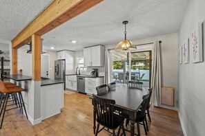 Una cocina moderna con una isla central, vigas de madera y un área de comedor con una mesa y sillas.
