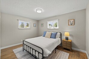 A bedroom with a bed, bedside table, lamp, two windows, and a ceiling light. - Spacious 4-bedroom House close to Lake Coeur d'Alene and Downtown (Coeur d'Alene)