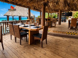 Un salon de restaurant doté d’un toit de chaume, de tables en bois, de chaises en osier et offrant une vue sur l’océan.