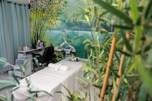 Une pièce comprenant un lit, un bureau, une chaise, une table de massage et donnant sur un plan d’eau.