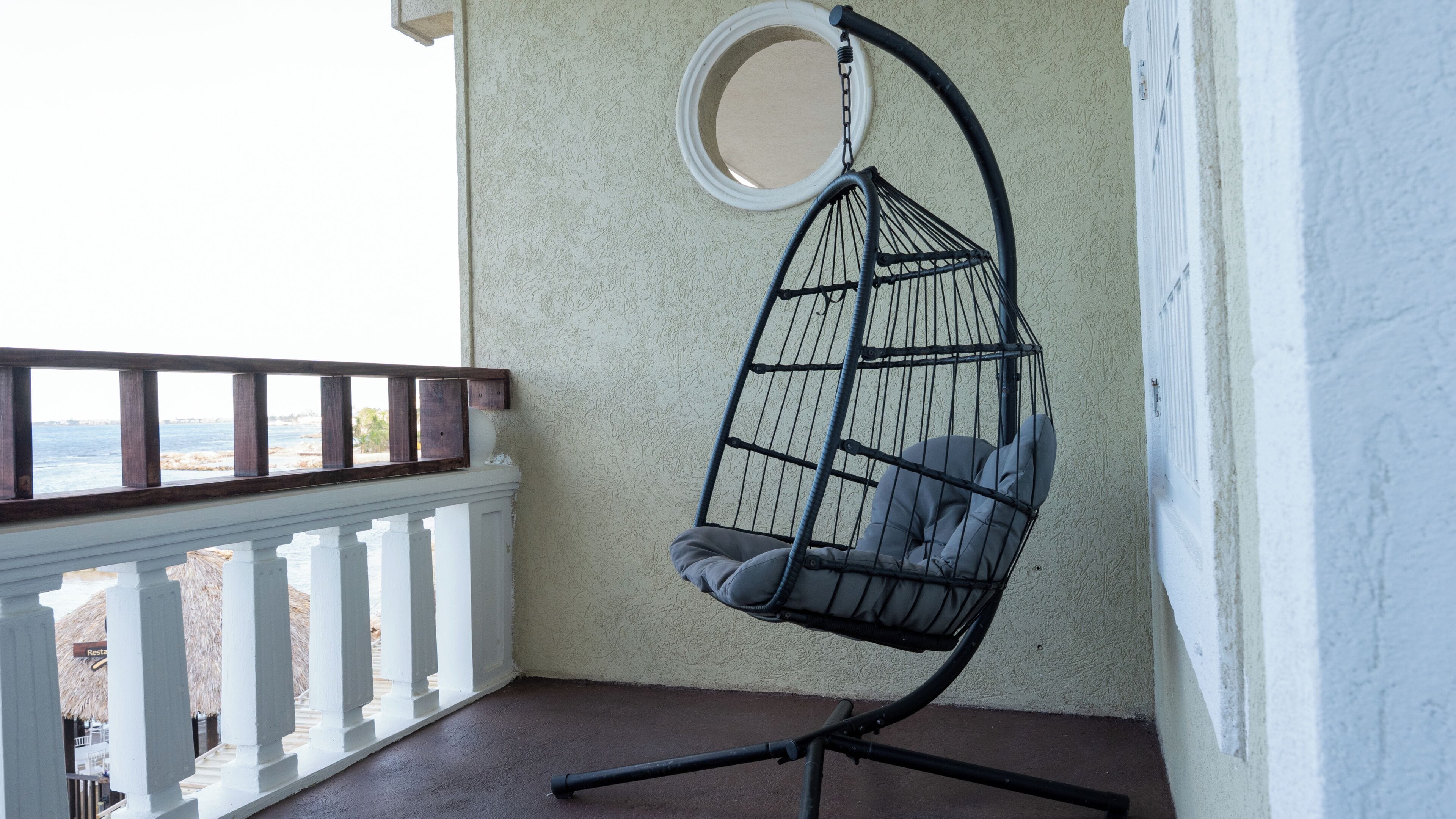 A hanging chair with cushions on a balcony with a railing and a view of the sea.