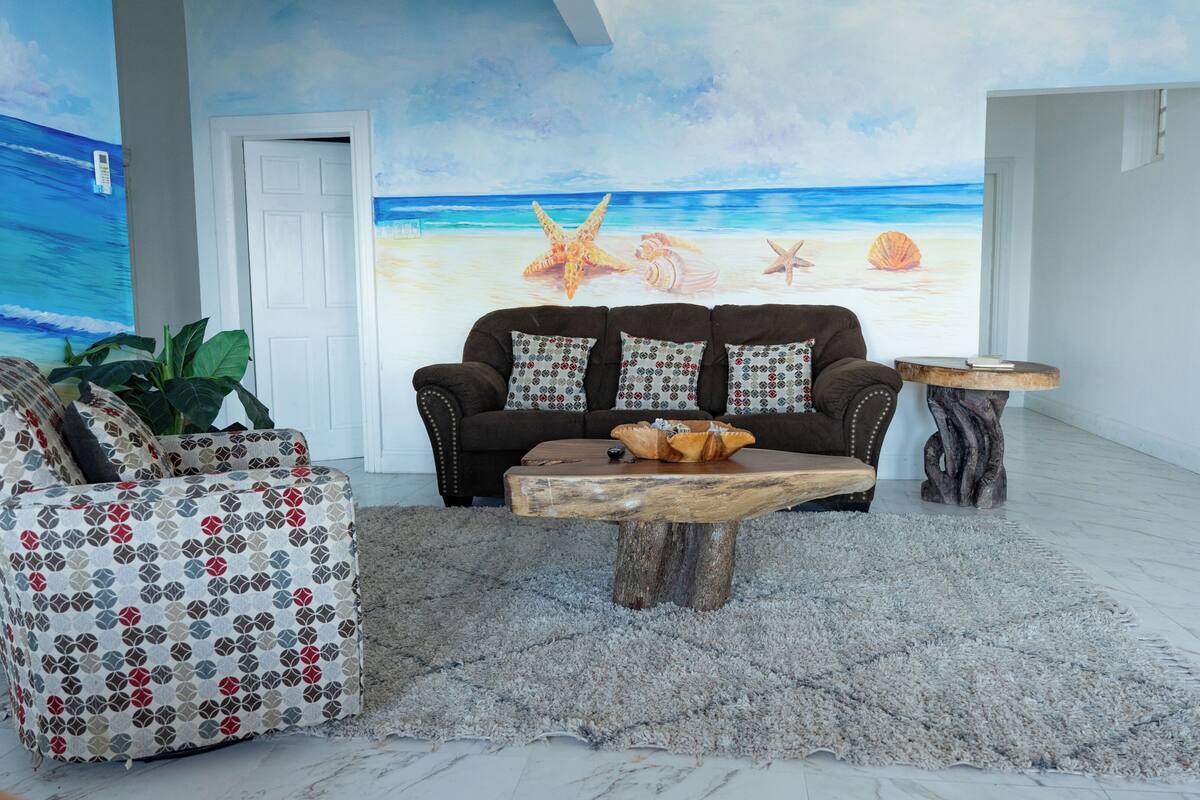 Una sala de estar con un mural de playa, un sofá marrón, un sillón estampado y una mesa de centro de madera.