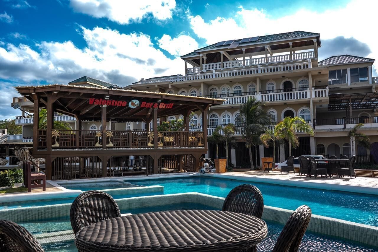 A pool area with lounge chairs, a bar named 'Valentine's Bar & Grill,' and a multi-story building with balconies.
