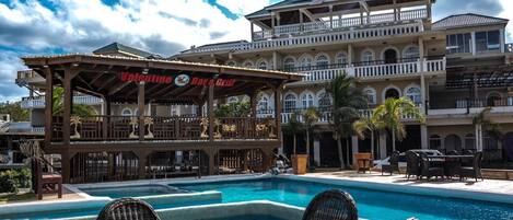 A pool area with lounge chairs, a bar named 'Valentine's Bar & Grill,' and a multi-story building with balconies.