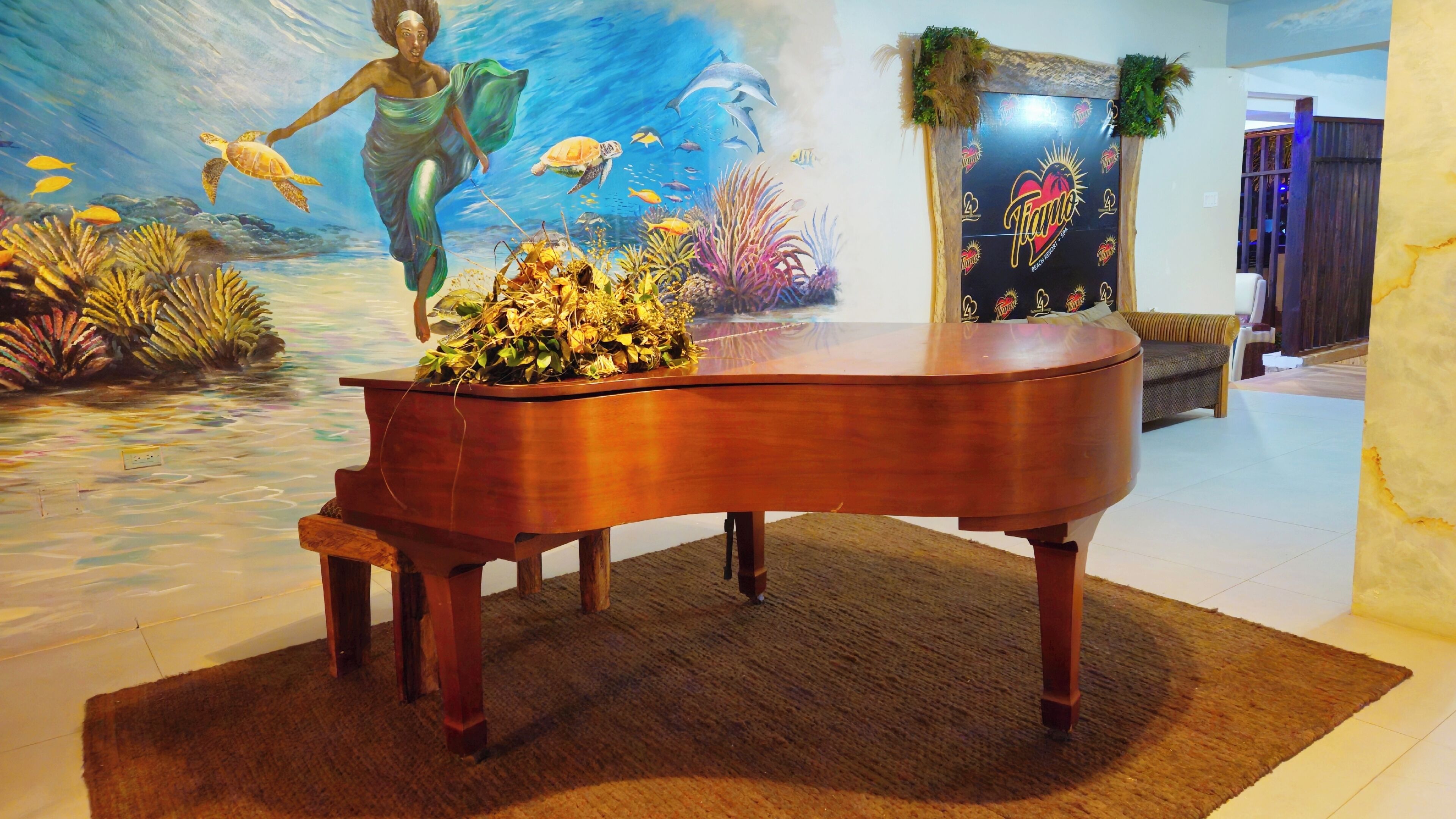 Een vleugelpiano in een kamer met een muurschildering van een onderwaterlandschap en een muur met een logo.