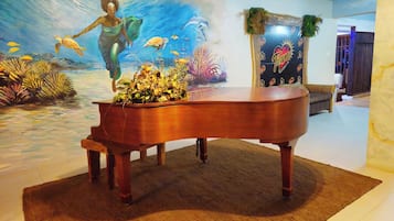 Een vleugelpiano in een kamer met een muurschildering van een onderwaterlandschap en een muur met een logo.