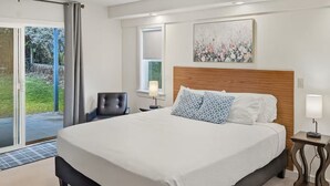 A hotel room with a large bed, a chair, a bedside table, a lamp, and a window with a view of greenery. - 2 for 1 Stay: Jacuzzi/Starlit Mtn Skies/Near Beach (Waimea)