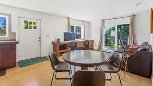 A modern living room with a dining table, chairs, a sofa, a TV, and a sliding glass door leading to a balcony. - 2 for 1 Stay: Jacuzzi/Starlit Mtn Skies/Near Beach (Waimea)